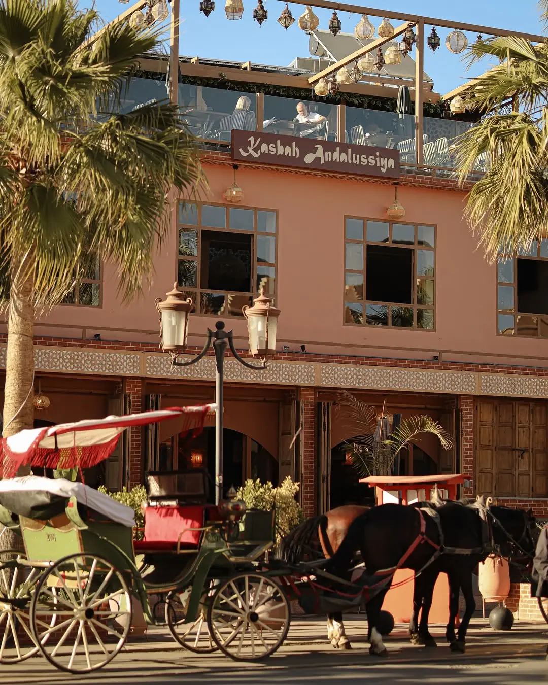 Horse-drawn calèches waiting outside the terracotta façade of Kasbah Andalussiya